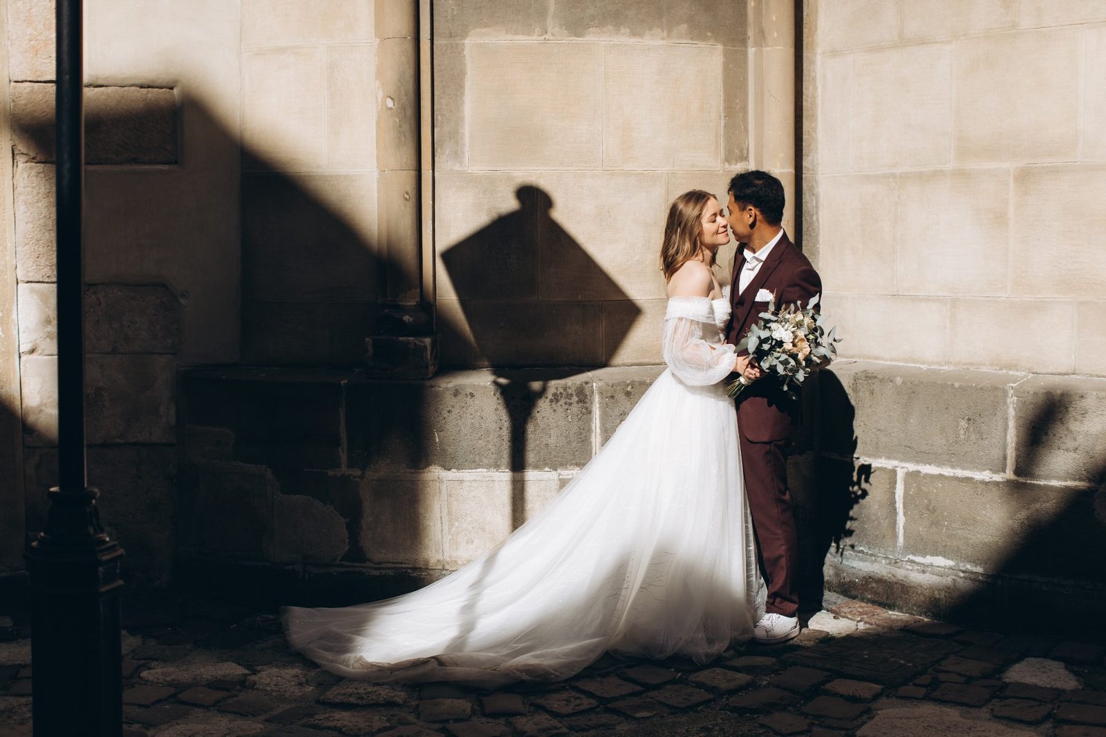 Wedding couple against a sunlit stone wall